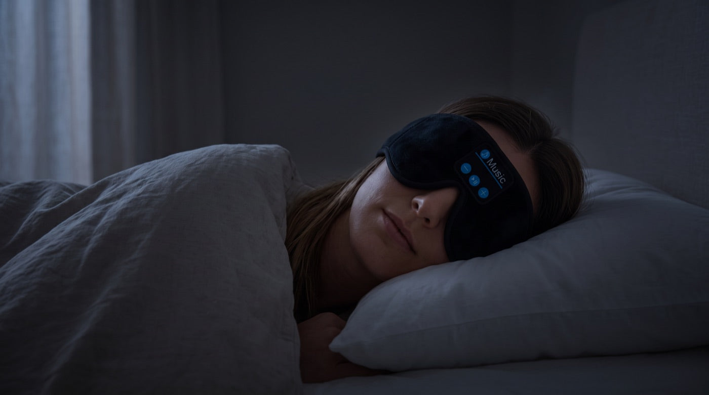 A woman asleep on her side in a dark room, wearing the DaySomnia headband.